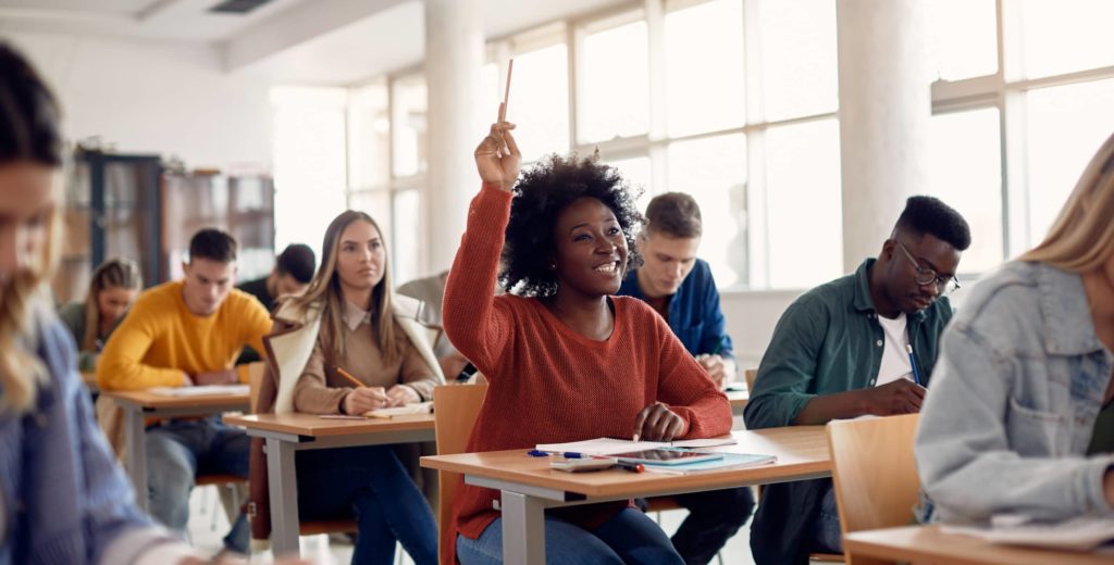 Happy student raising arm to answer question while attending class with her university colleagues.